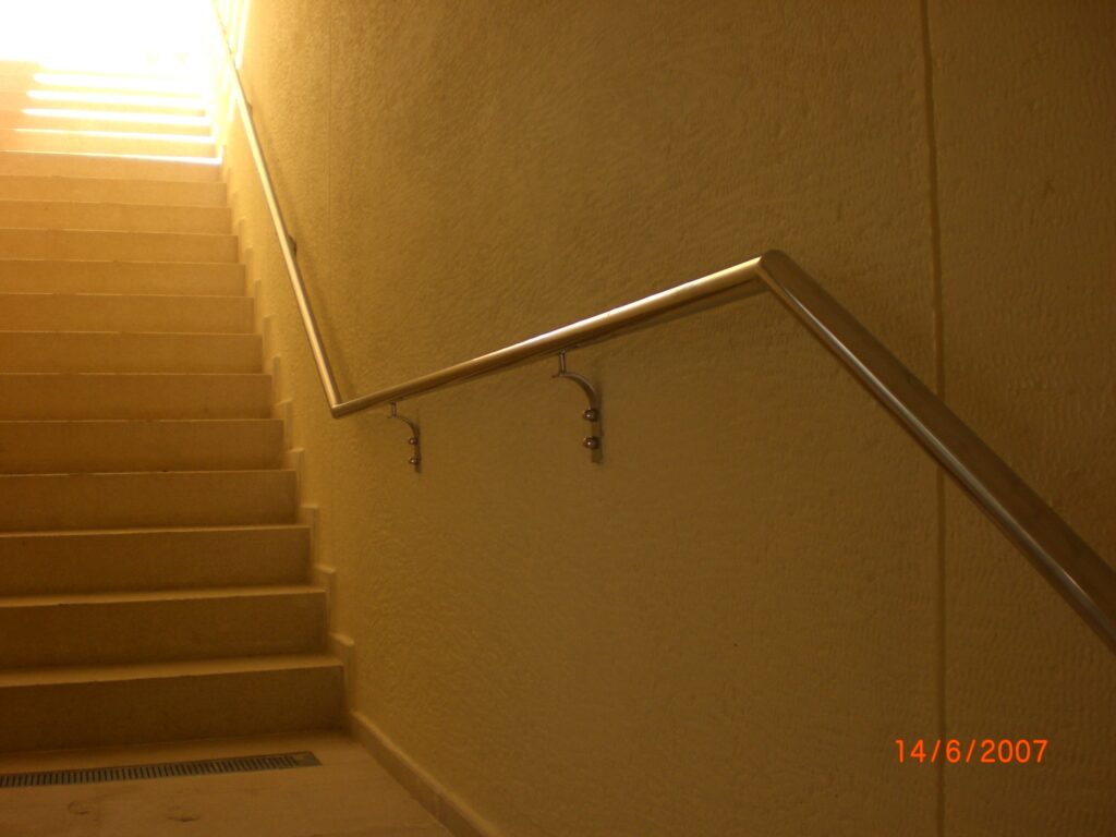 ARC-MOD-08_14: Wall-mounted brushed stainless steel handrail with custom standoff brackets on interior circulation staircase